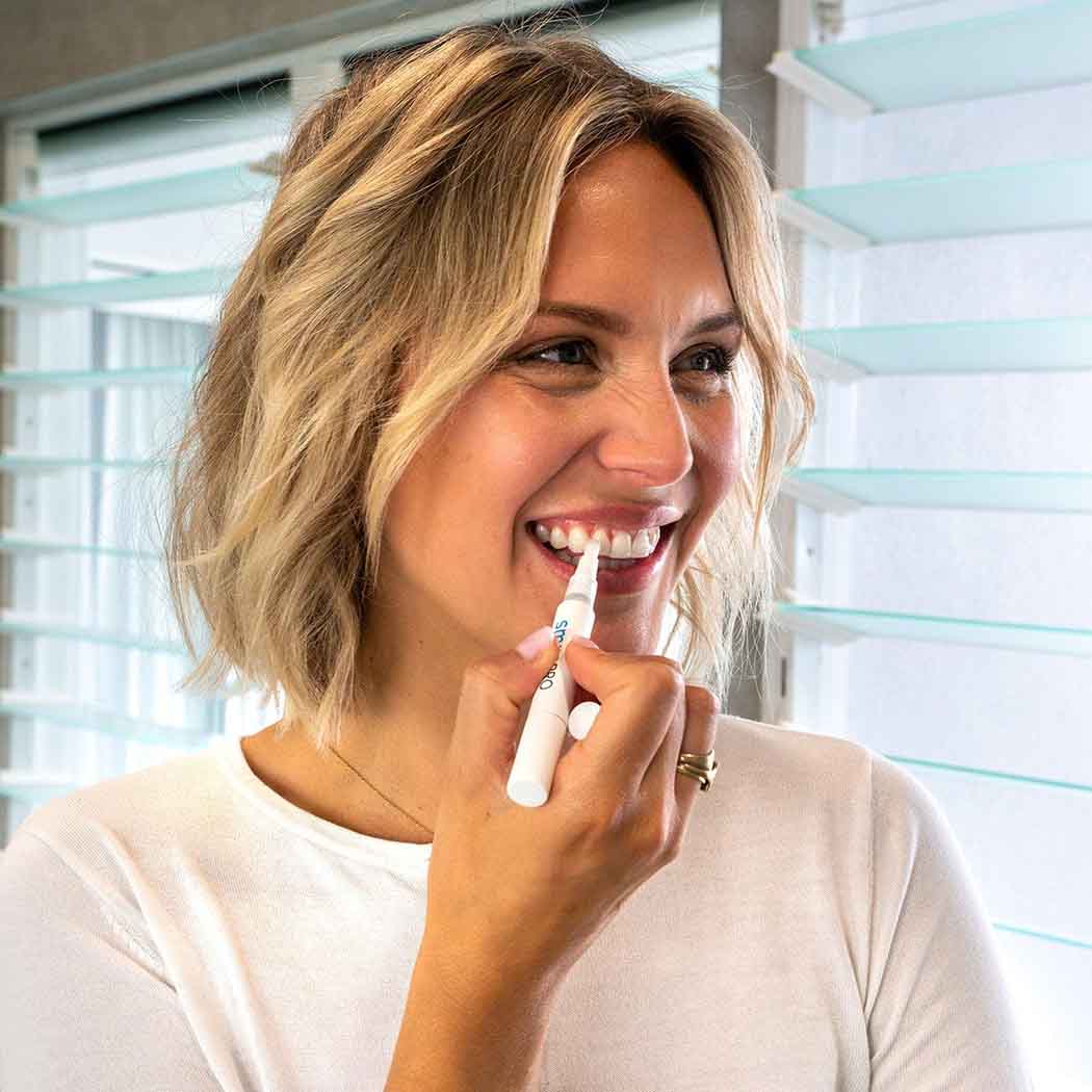 Kvinna som ler medan hon använder SmilePro-pennan för tandblekning